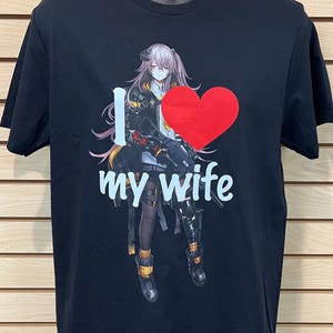 May include: Black t-shirt featuring an anime-style illustration of a woman with pink hair, a red heart, and the text "I love my wife" in white. The shirt is displayed on a mannequin.