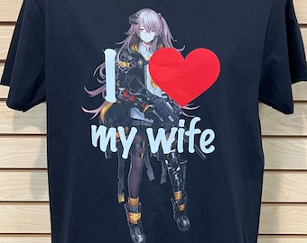 Puede incluir: Camiseta negra con una ilustración de estilo anime de una mujer con pelo rosa, un corazón rojo y el texto "I love my wife" en blanco. La camiseta se muestra en un maniquí.