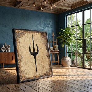 May include: A rectangular framed wall art piece featuring a black trident symbol centred on a textured, beige, and distressed background. The artwork is enclosed in a thin black frame, showcasing a weathered, aged appearance with dark brown edges.