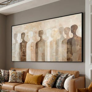 Könnte beinhalten: Abstraktes Gemälde mit einer Reihe von silhouettenhaften Figuren in verschiedenen Braun- und Beigetönen. Das Kunstwerk ist in Schwarz gerahmt und hängt über einem braunen Ledersofa mit dekorativen Kissen. Die gedämpften Farbtöne erzeugen eine beruhigende Ästhetik.