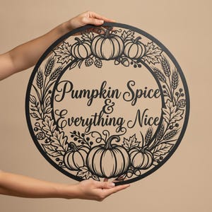 Könnte beinhalten: Ein rundes Wandbild aus schwarzem Metall mit einem ausgeschnittenen Design aus Kürbissen, Weizenähren und Herbstblättern. Der mittlere Text lautet "Pumpkin Spice & Everything Nice" in Schreibschrift. Der Rand besteht aus botanischen Elementen.