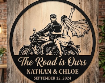 May include: A circular black metal wall sign featuring a cutout illustration of a person driving a motorcycle with a passenger in a wedding dress and veil. The text reads The Road is Ours, NATHAN & CHLOE, and SEPTEMBER 12, 2024.