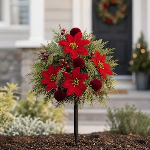 May include: A decorative garden stake featuring a spherical topiary arrangement of green cedar foliage, vibrant red poinsettia flowers, small red berries, and dark red velvet spheres, all supported by a slender black metal stake.