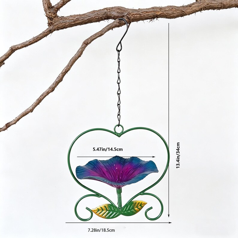 May include: A hanging bird feeder shaped like a heart, with a purple and blue flower-shaped bowl. The feeder is 13.4 inches tall and 7.28 inches wide, with a 5.47-inch bowl. It is suspended by a chain and hook from a tree branch.