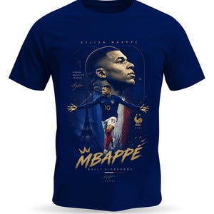 May include: A navy blue t-shirt featuring a graphic of Kylian Mbapp&eacute;. The design includes a portrait, a full-body action shot, the text "KYLIAN MBAPPE", "VITESSE MENTALITE LEGENDE", "BUILT DIFFERENT", a crown icon, and the French Football Federation logo.