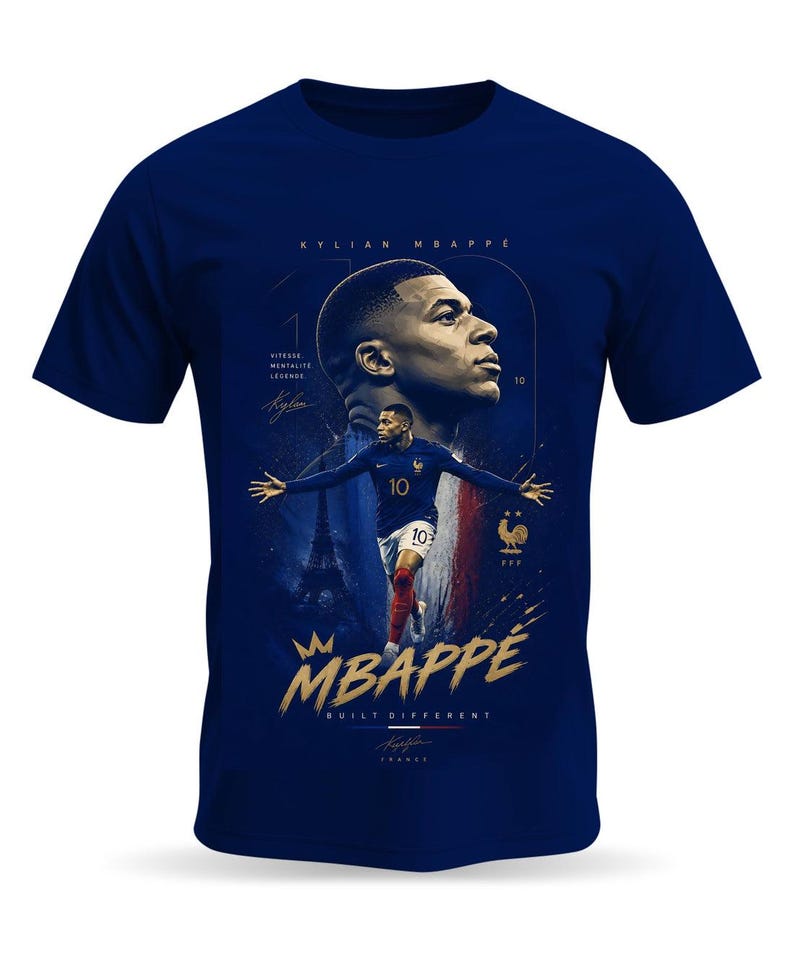 May include: A navy blue t-shirt featuring a graphic of Kylian Mbapp&eacute;. The design includes a portrait, a full-body action shot, the text "KYLIAN MBAPPE", "VITESSE MENTALITE LEGENDE", "BUILT DIFFERENT", a crown icon, and the French Football Federation logo.