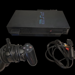 May include: A black PlayStation 2 console with a matching controller and cables. The console has the text "PS2" in blue and the Sony logo. The controller has multiple colored buttons and a directional pad.