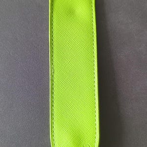 May include: A lime green pen pouch with a textured surface and rounded ends. The accessory features visible stitching along the edges and the embossed text MONTBLANC with a small circular logo symbol located near the bottom of the front side.