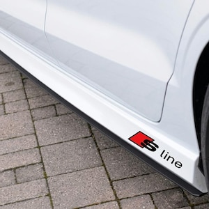 Peut inclure: Un bas de caisse de voiture blanc avec un autocollant emblème S line noir et rouge. L'autocollant présente un carré rouge avec un S noir et le mot line en texte noir. La carrosserie est blanche avec une garniture noire et des roues noires.