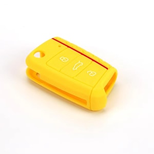 Könnte beinhalten: Eine leuchtend gelbe Autoschlüsselhülle aus Silikon in rechteckiger Form mit abgerundeten Ecken. Die Hülle zeigt drei weiße, geprägte Symbole für Verriegeln, Entriegeln und Kofferraumöffnung sowie einen dünnen roten Streifen am oberen Rand.