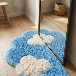 May include: A plush, cloud-shaped area rug featuring a textured blue background with two soft, cream-colored cloud motifs. The rug is positioned partially underneath a tall, rectangular floor mirror, creating a reflective effect on the surface.