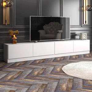 May include: A modern living room featuring a large flat-screen TV above a long, white cabinet. The room has dark gray paneling, gold wall sconces, and a wooden floor with a herringbone pattern. A small clock and decorative sculpture are also visible.