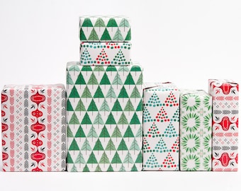 Può includere: Una collezione di regali confezionati con vari motivi festivi. I regali sono avvolti in carta bianca con disegni tra cui alberi di Natale verdi, ornamenti rossi e verdi e forme geometriche. I regali sono disposti su uno sfondo bianco.