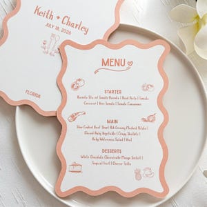 Może przedstawiać: Menu weselne i osobna karta z imionami "Keith + Charley" oraz datą "18 lipca 2026" w miękkim koralowym kolorze. Menu ma falisty brzeg i zawiera przystawki, dania główne i desery. Słowo "MENU" znajduje się na górze.