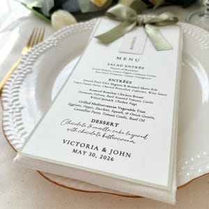 Sage green satin ribbon wedding menu card with attached place card and green bordered design on elegant table setting