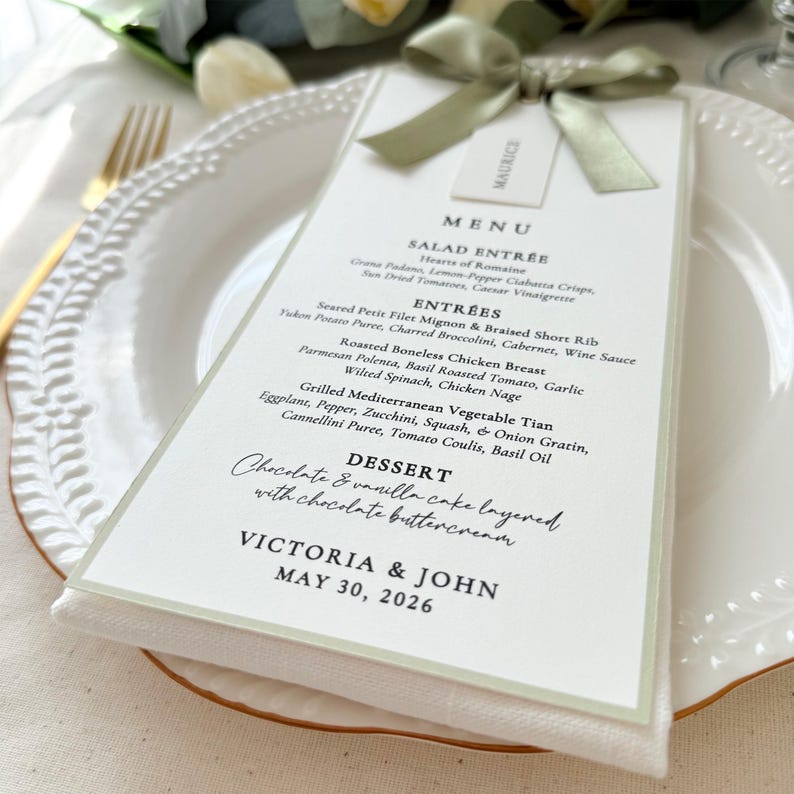 Sage green satin ribbon wedding menu card with attached place card and green bordered design on elegant table setting