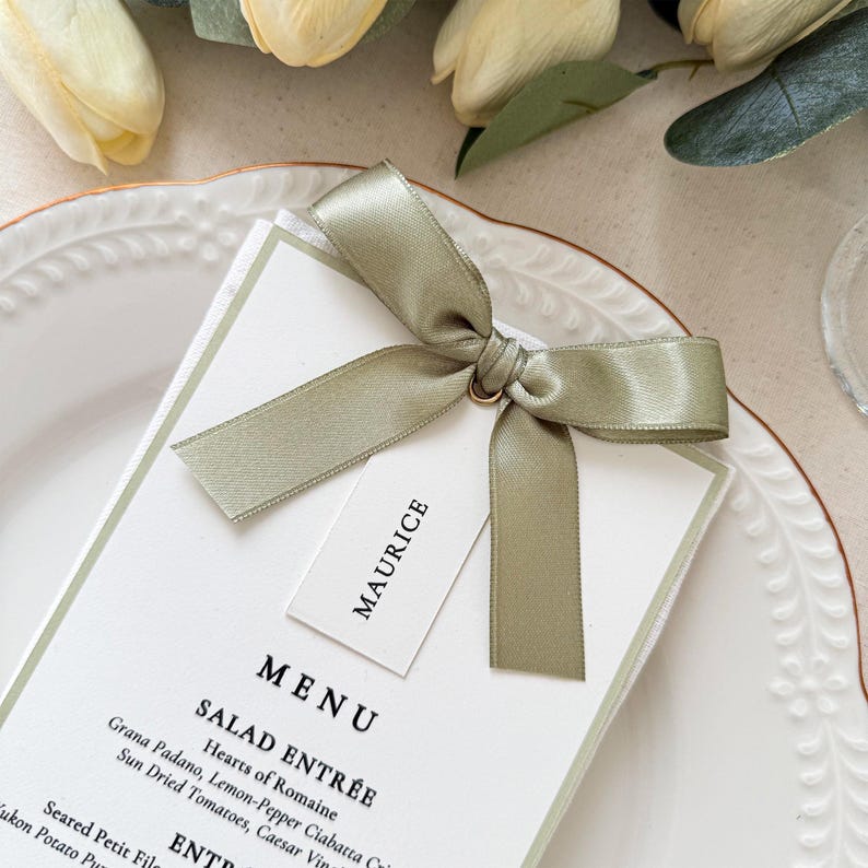 Close up of sage green satin ribbon bow with personalized place card on printed wedding menu card