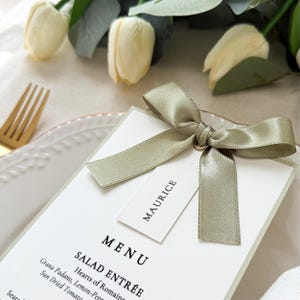 Sage green ribbon bow menu card with name tag styled on wedding place setting with soft floral details