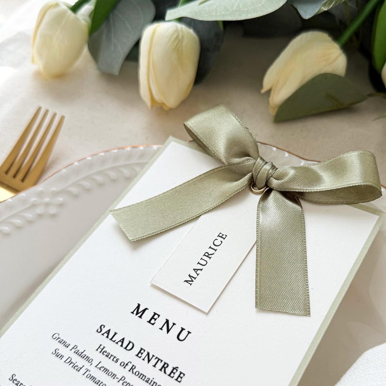 Sage green ribbon bow menu card with name tag styled on wedding place setting with soft floral details