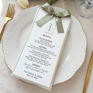 Personalized wedding menu card with sage green satin ribbon bow and guest name tag on white dinner plate