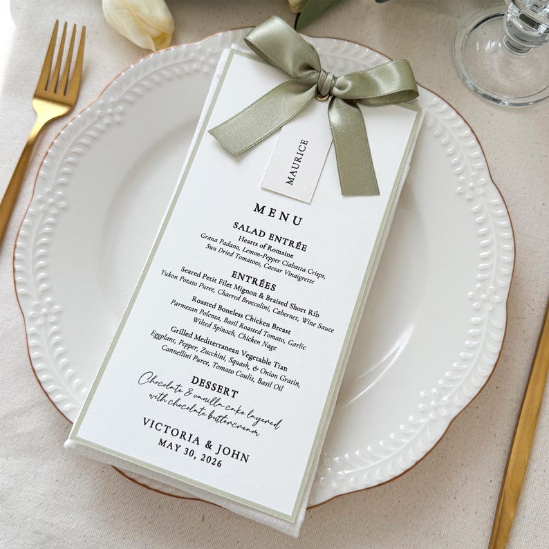 Personalized wedding menu card with sage green satin ribbon bow and guest name tag on white dinner plate