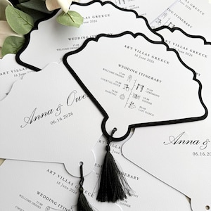 May include: White wedding itinerary cards with a black scalloped border and black tassel. The cards feature the names "Anna & Owe" and the date "06.16.2026". The itinerary includes times for welcome drinks, cocktail hour, ceremony, dinner, and dancing.