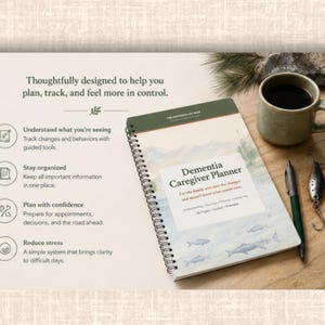 May include: A spiral-bound Dementia Caregiver Planner with a green and white cover, a mug of coffee, a pen, and a fishing lure on a wooden surface. The planner's cover features a watercolor illustration of fish.