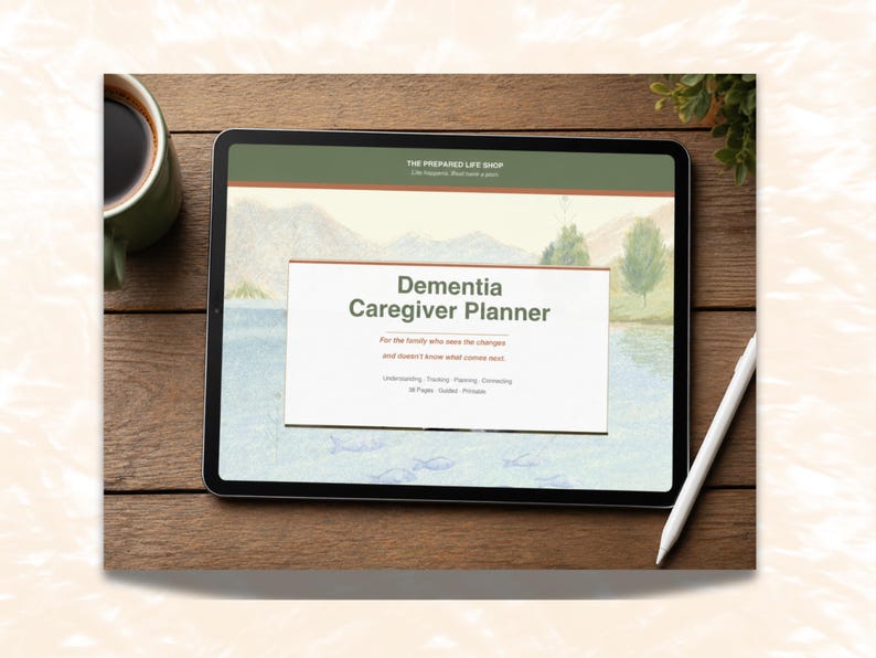 May include: A digital tablet displays a "Dementia Caregiver Planner" with a landscape background. The tablet is on a wooden surface, next to a cup of coffee, a white stylus, and a small plant. The planner's text includes "Understanding, Tracking, Planning, Connecting."