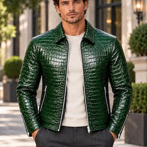 Puede incluir: Una chaqueta de color verde esmeralda brillante con un patrón texturizado de piel de cocodrilo, que presenta un cuello puntiagudo, una cremallera frontal plateada completa, bolsillos y puños con cremallera, sobre una camiseta blanca y pantalón gris.