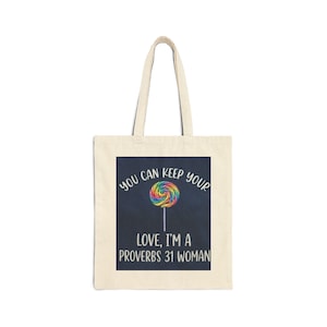 Puede incluir: Bolso tote color crema con un cuadrado azul oscuro que presenta un gráfico de piruleta colorido. El texto dice "YOU CAN KEEP YOUR LOVE, I'M A PROVERBS 31 WOMAN" en blanco, curvado alrededor de la piruleta y debajo.