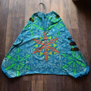 May include: Loose-fitting trousers in a vibrant blue hue featuring a repeating geometric flower pattern in bright lime green and a central star-shaped motif in orange. The garment includes an elasticized drawstring waistband and side pockets.