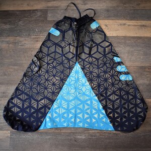 May include: Wide-leg trousers featuring a dark navy and grey geometric flower-of-life pattern. The garment includes a large, bright blue triangular panel on the front, an elasticized drawstring waistband, and side pockets with black zipper closures.