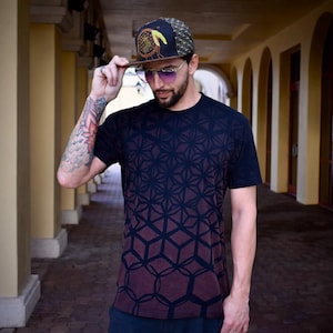 May include: A dark maroon t-shirt featuring a black geometric pattern of interlocking circles and cubes. The shirt is paired with a dark baseball cap displaying a yellow dreamcatcher graphic and a pair of sunglasses with purple-tinted lenses.