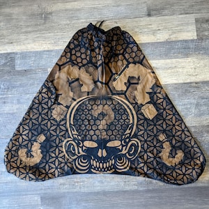 May include: Loose-fitting trousers featuring a black and tan geometric pattern with a repeating flower of life motif. The design includes a central stylized skull graphic, an elasticized drawstring waistband, and side pockets with zipper closures.