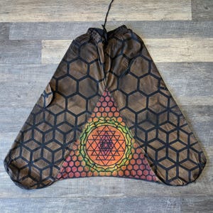 May include: Brown harem pants featuring a black geometric honeycomb pattern across the fabric. A large triangular panel at the center displays a vibrant, multi-colored Sri Yantra mandala design with orange, yellow, and red hues, finished with a drawstring.