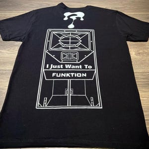 Puede incluir: Una camiseta negra de manga corta con un estampado gráfico blanco de una caja de altavoz grande. Sobre el altavoz hay un signo de interrogación blanco que gotea. El texto "I Just Want To FUNKTION" está impreso en blanco sobre el diseño.