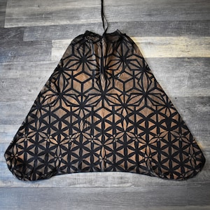 May include: A pair of loose-fitting trousers featuring a repeating black geometric pattern of intersecting circles and lines over a bronze-colored background. The garment has a gathered elastic waistband with a drawstring and a wide, flared leg design.