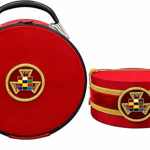 Op de afbeelding: Twee rode koffers, een ronde met een handvat, de andere cilindrisch. Beide hebben gouden randen en een gouden embleem met gekleurde vierkanten. De grotere koffer heeft een zwart handvat. De kleinere heeft gouden touwrand.