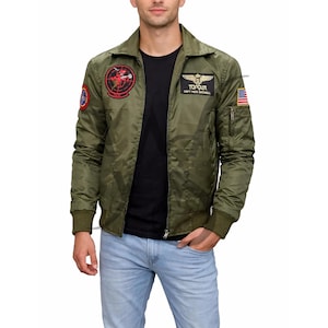 Op de afbeelding: Olijfgroene bomberjack met meerdere patches, waaronder een cirkelvormig embleem en een Amerikaanse vlag. De jas heeft een ritssluiting, geribde manchetten en de tekst "TOP GUN CAPT. PETE MITCHELL".