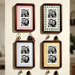 Op de afbeelding: Vier rechthoekige wandlijsten van donker hout, elk met een verticale zwart-wit fotostrip van een koppel. De lijsten hebben achtergronden met patronen in roze, groen, blauw en geel. Elke lijst heeft twee gouden haakjes met een belletje.