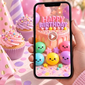 May include: A smartphone screen displaying a digital image of a pink birthday cake with the text HAPPY BIRTHDAY in pink letters, surrounded by colorful smiling spherical characters, small stars, and confetti on a light pink background.