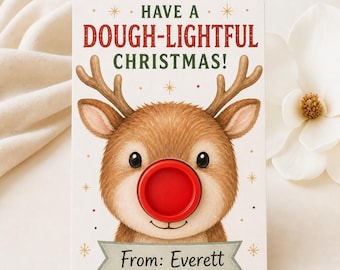 Może przedstawiać: Prostokątna kartka świąteczna z ilustracją brązowego renifera z czerwonym, okrągłym nosem. Tekst głosi HAVE A DOUGH-LIGHTFUL CHRISTMAS! oraz From: Everett. Kartka ma białe tło ozdobione małymi złotymi gwiazdkami.