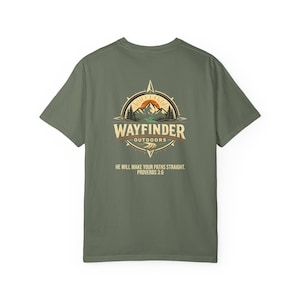 May include: Olive green t-shirt with a compass design. The design includes the words "WAYFINDER OUTDOORS" and the text "HE WILL MAKE YOUR PATHS STRAIGHT. PROVERBS 3:6." The design features mountains, trees, and a sun.
