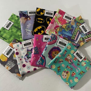 May include: A collection of nine folded 18 in. by 21 in. 100% cotton fat quarter fabric squares featuring various colorful character and graphic prints, including Batman, Minecraft, Teenage Mutant Ninja Turtles, Peppa Pig, and JoJo Siwa.