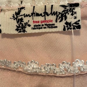 May include: Close-up of a light pink garment with white lace trim. A tag with the text "Intimately Free People" is visible. The tag also includes the text "Made in Vietnam" and "Fabriqu&eacute; en Vietnam".
