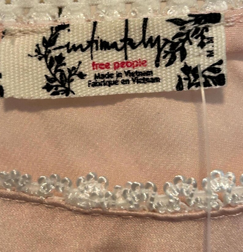 May include: Close-up of a light pink garment with white lace trim. A tag with the text "Intimately Free People" is visible. The tag also includes the text "Made in Vietnam" and "Fabriqu&eacute; en Vietnam".
