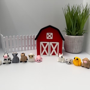 May include: A collection of miniature farm animal figurines, including a chicken, cow, pig, and sheep, arranged in front of a red barn model. A white picket fence and a potted plant complete the farm scene.