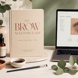 Può includere: Un'immagine still life con un libro intitolato "The Brow Masterclass" con testo marrone. Un laptop mostra le istruzioni per il brow mapping. Sono presenti anche una bottiglia di siero per sopracciglia, una piccola ciotola e un pennello per il trucco.