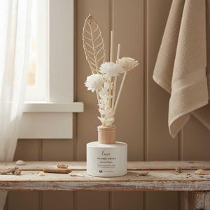 May include: A white ceramic diffuser with a wooden collar and decorative floral arrangement. The diffuser has the text "Luxe Island Crush" and is displayed on a rustic wooden surface. A beige towel hangs in the background.
