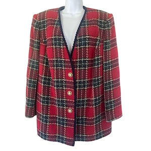 May include: A long-sleeved blazer featuring a red, black, and gold plaid pattern. The garment has a deep V-neckline trimmed with dark navy blue braided piping and is fastened with three circular gold-toned buttons down the front center.